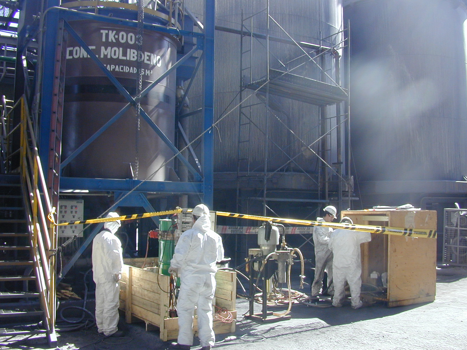 Crew spray-applying protective coating to large process storage tanks at an industrial plant