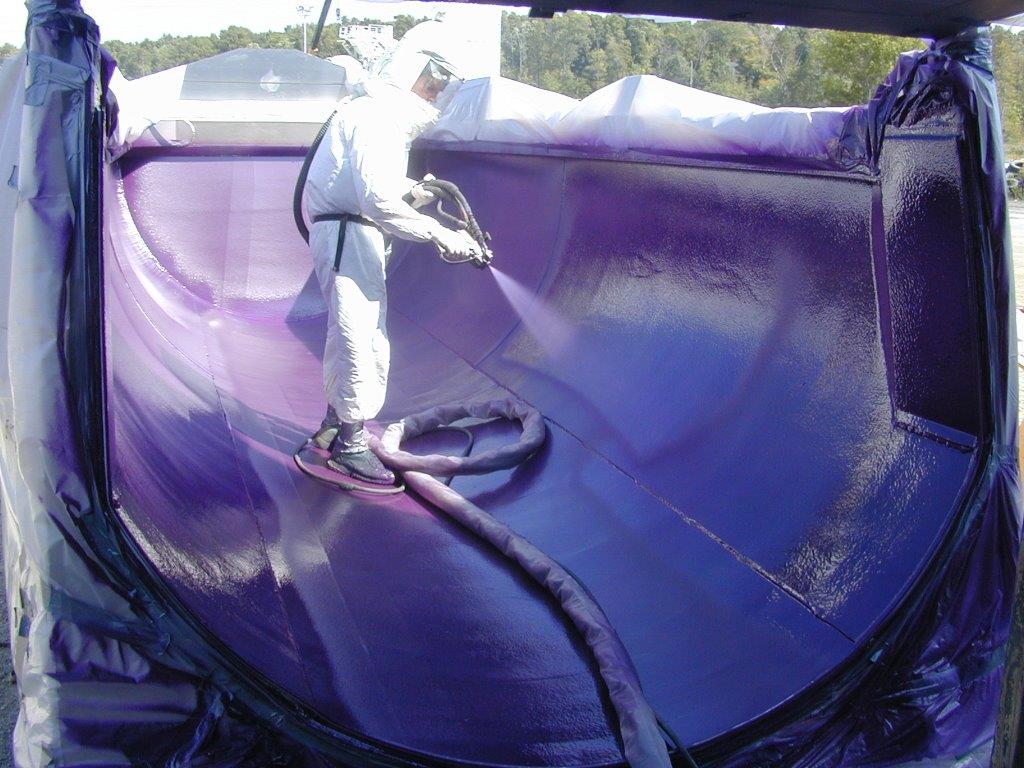 Applicator in full protective gear spray-applying polyurea to the inside of a large truck body