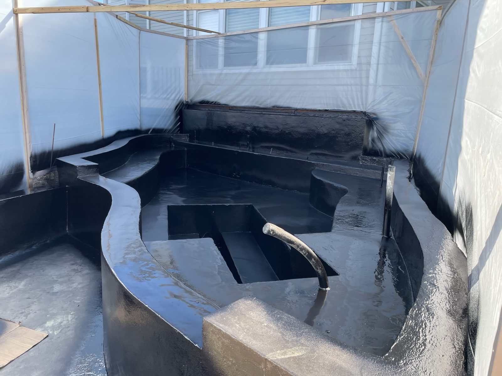 Seamless black spray-applied waterproofing membrane covering formed concrete walls, steps and floor in one continuous layer