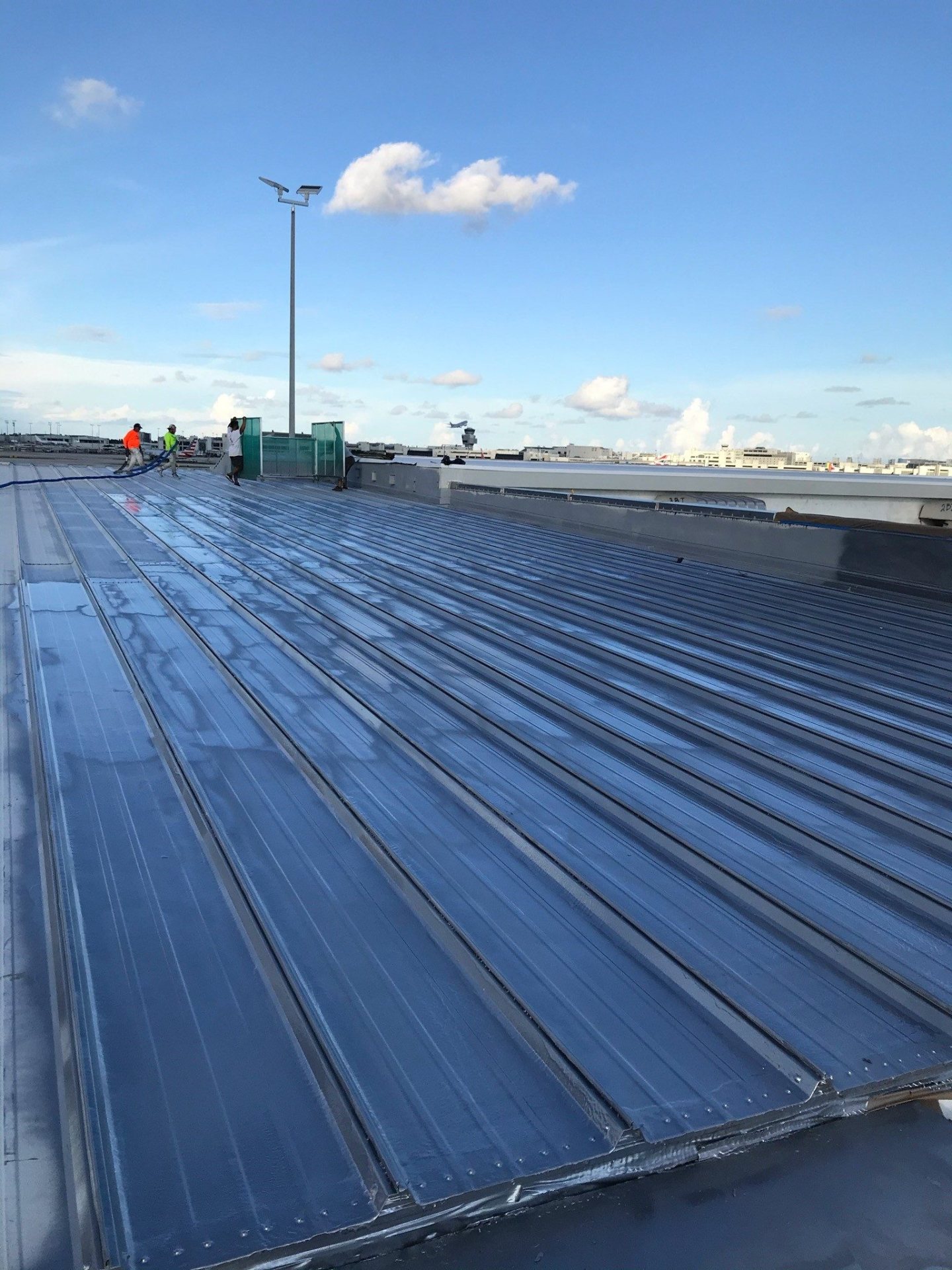Freshly spray-applied polyurea roof coating across a standing-seam metal roof, crew working at the far end