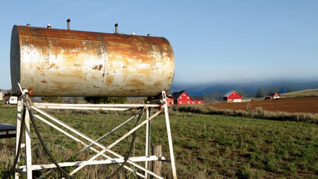Weathered farm fuel storage tank on a stand beside a red barn