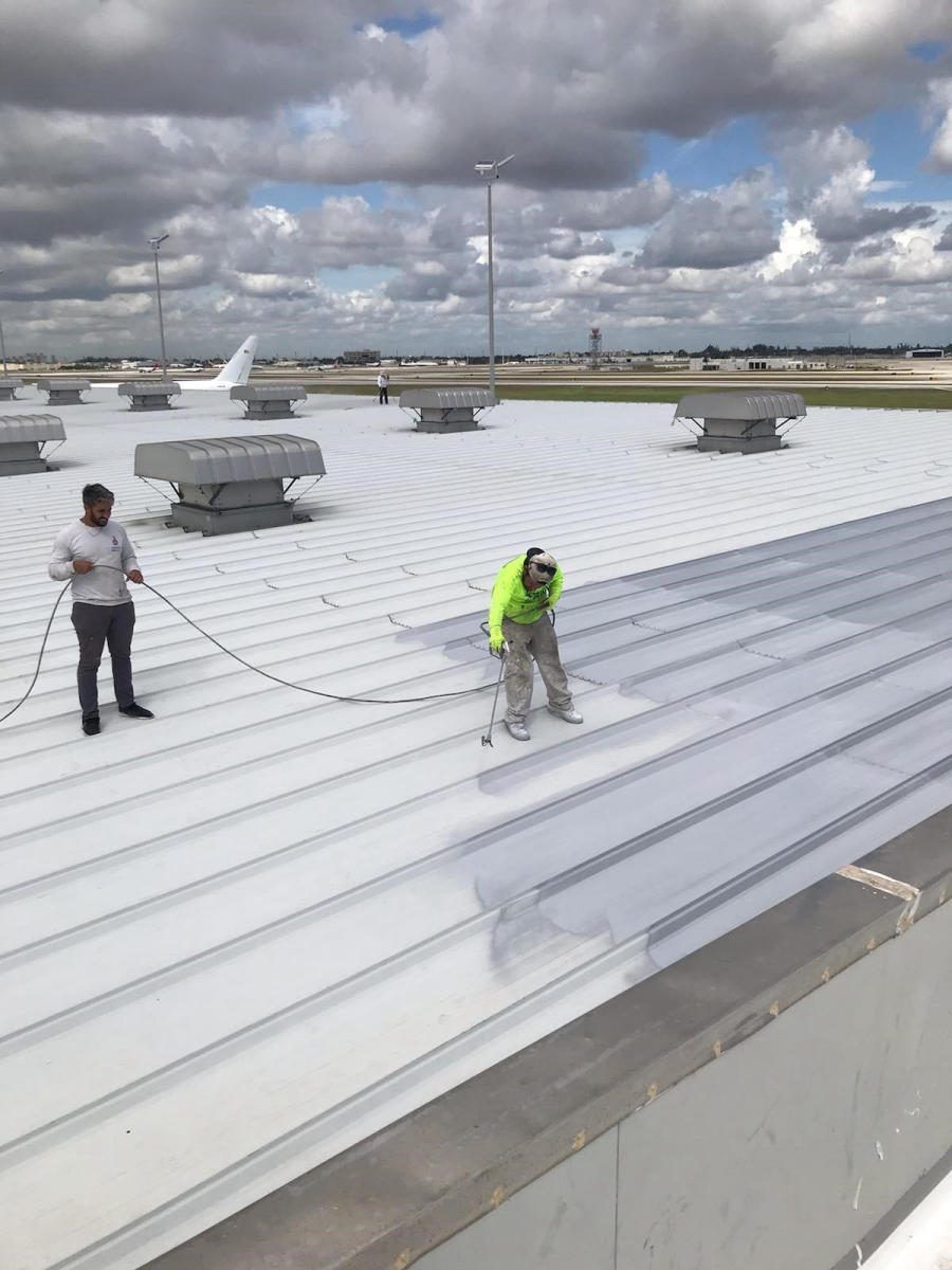 Crew spraying pure polyurea roof membrane on a standing-seam metal roof