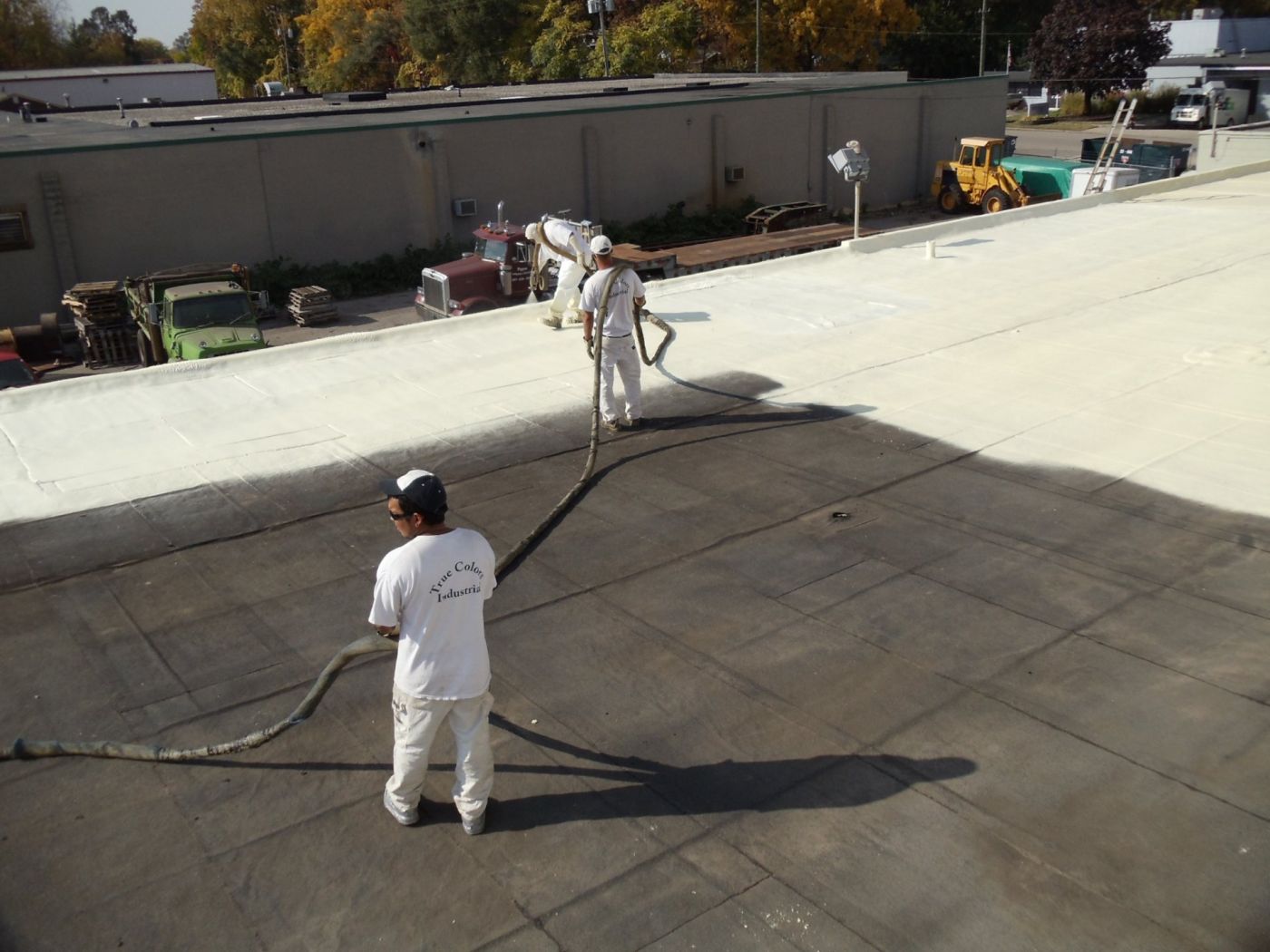 Applicators spraying a white membrane over a dark existing flat roof