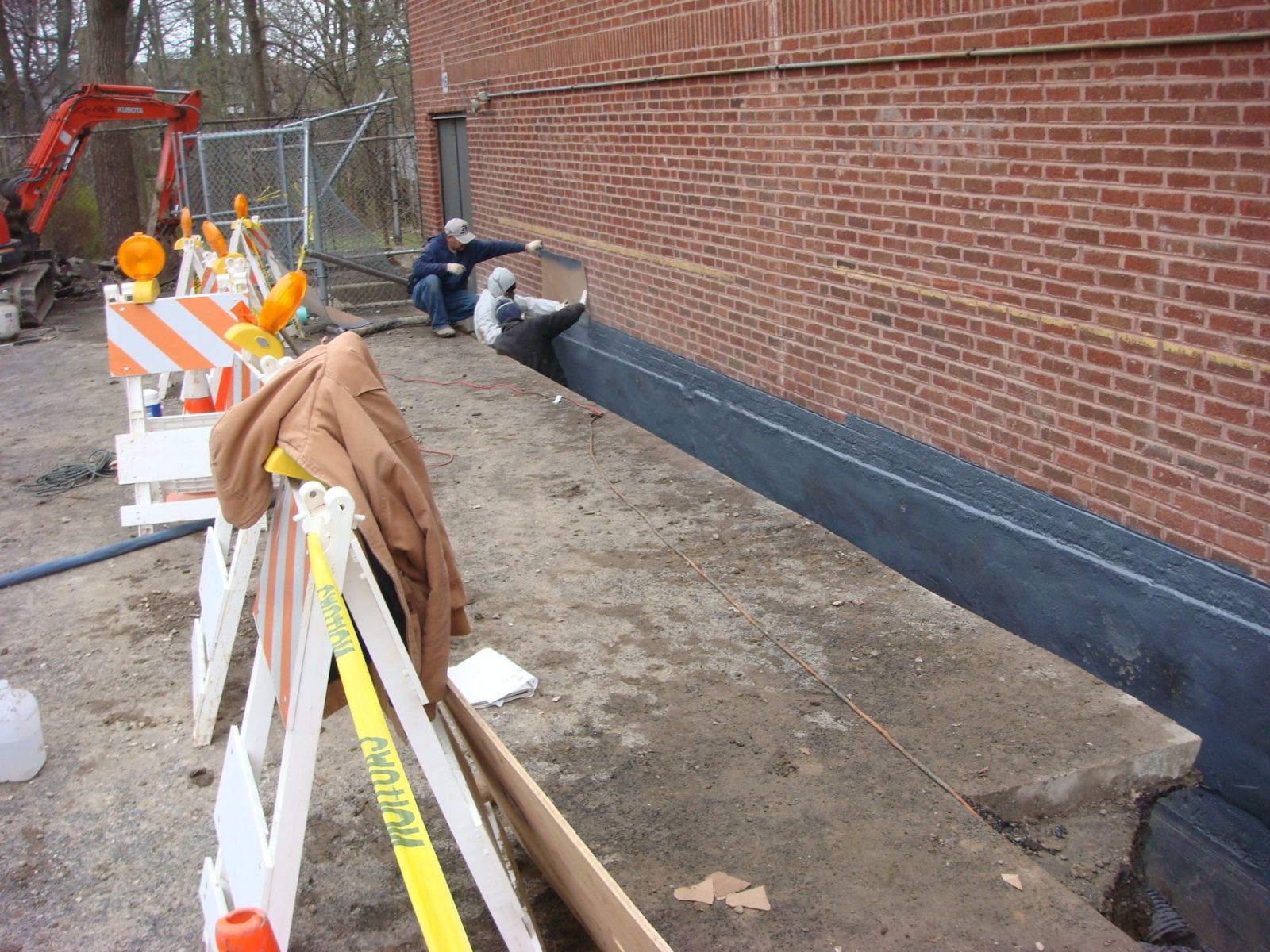 Applicator spraying Badger Black on a foundation wall in an open excavation