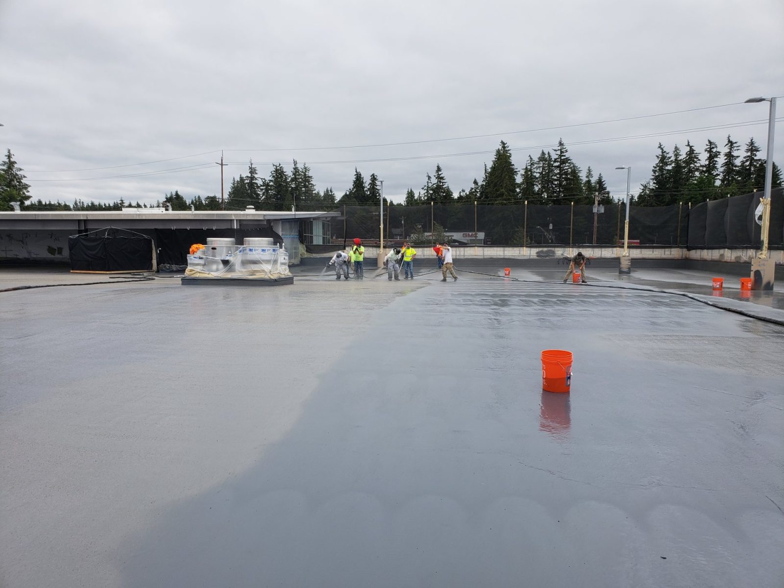 Crew applying a seamless polyurea waterproofing membrane across a large flat commercial roof