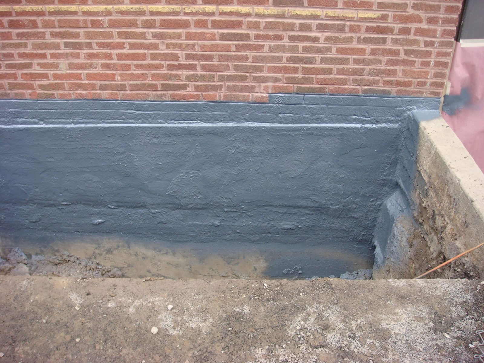 Polyurea waterproofing membrane on a below-grade brick foundation wall, ready for backfill