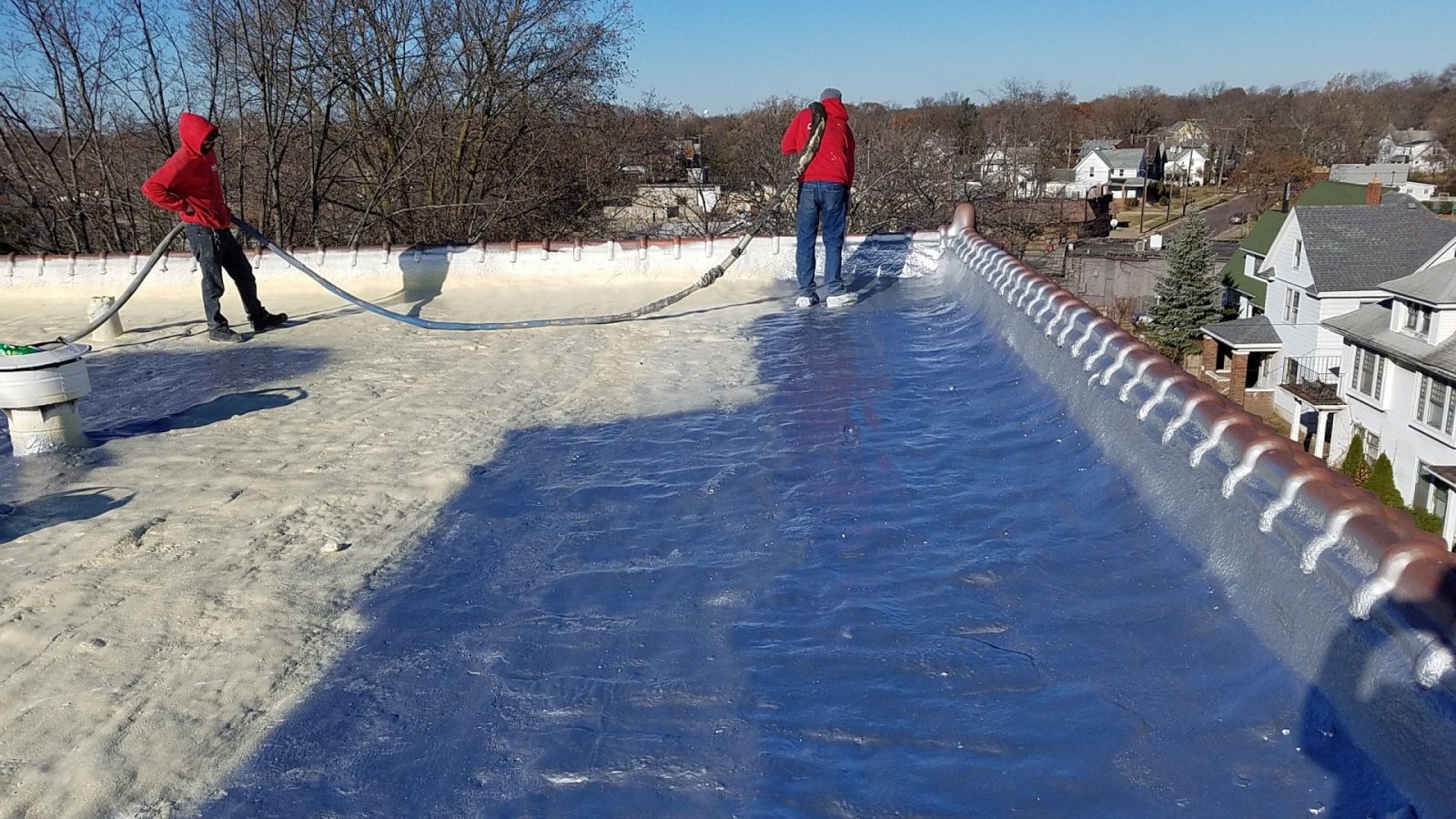Crew spraying polyurethane foam roofing on a commercial flat roof