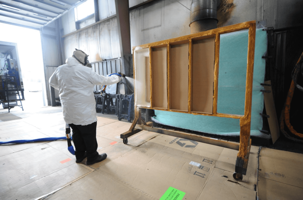 Oak Ridge employee wearing full protective gear spray test area with spray foam insulation